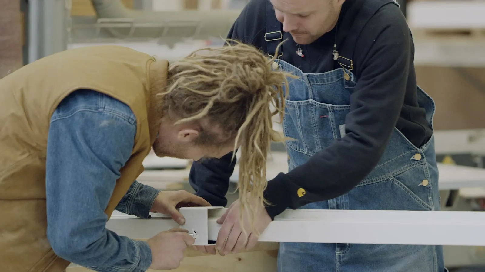 Twee makers gebogen over hetzelfde stuk hout aan de werkbank in de fabriek van Piet Hein Eek